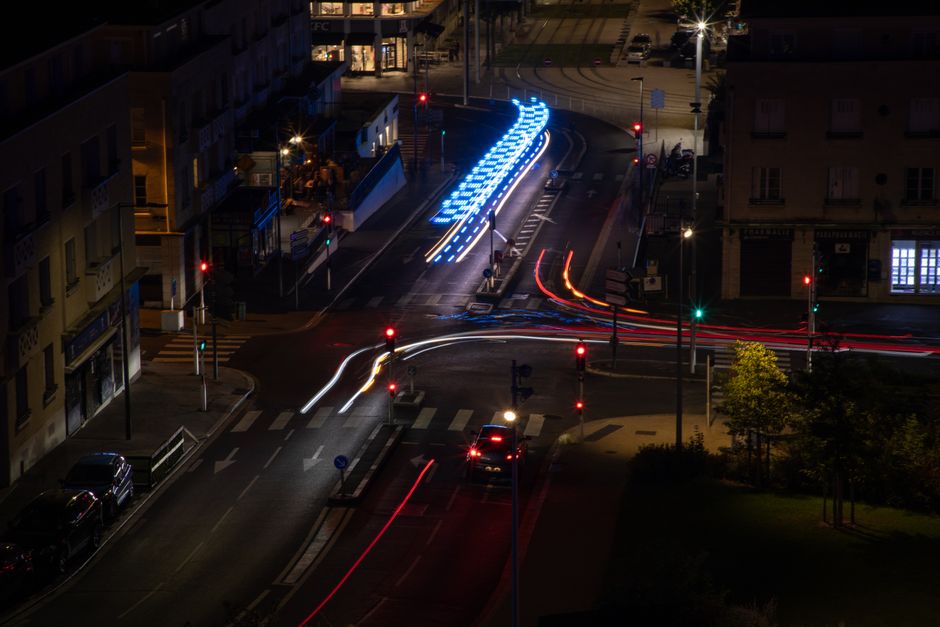 Aerial view of Caen's illuminated streets at night, showcasing colorful light trails and urban architecture.