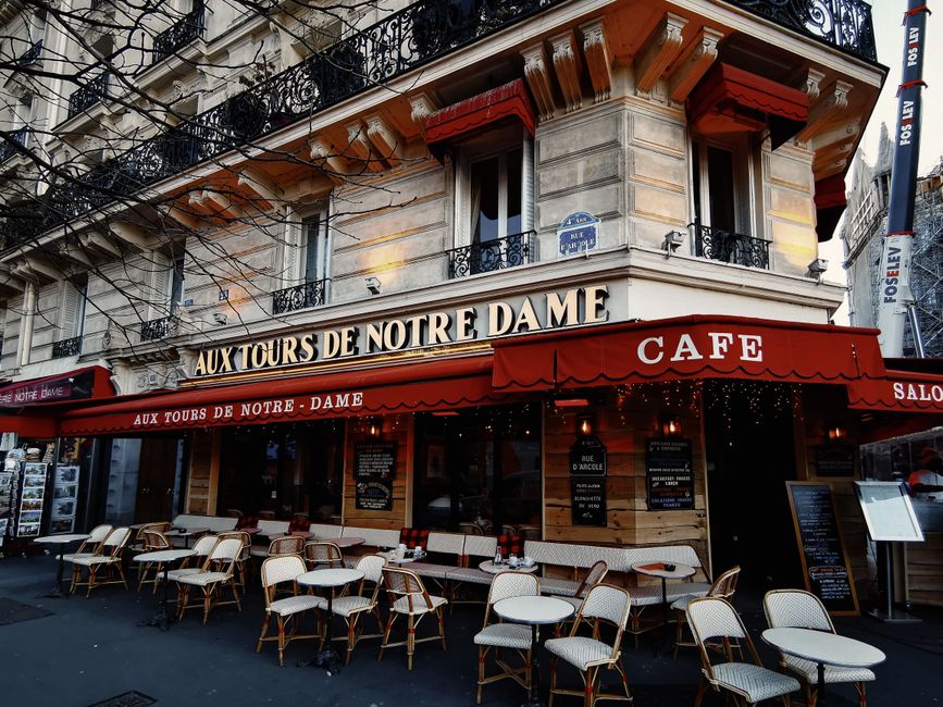 Parisian cafe Aux Tours de Notre Dame with empty outdoor seating in a vibrant urban setting.