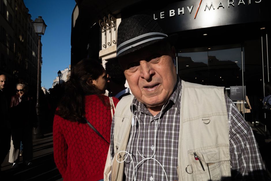 An elderly man in a summer street wearing a hat, captured during a sunny day in a bustling city.