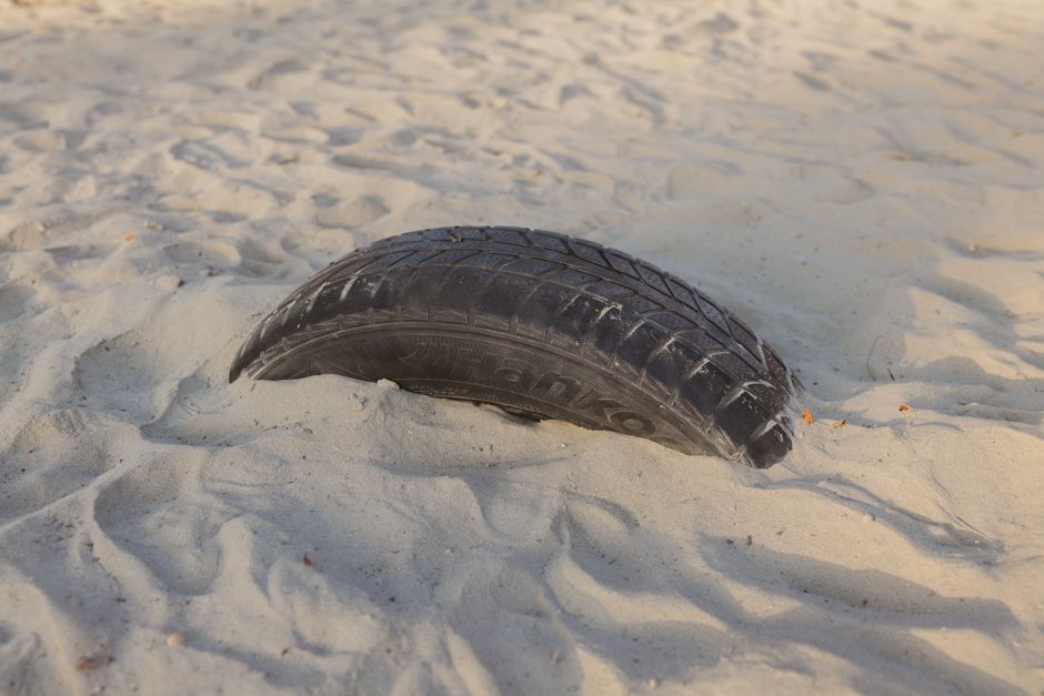 Close-up of a car tire partially buried in sand, evoking adventure.