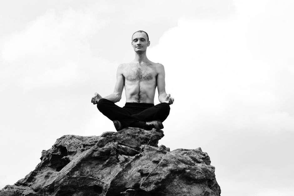 Shirtless man meditates cross-legged atop a rock in La Capelle-et-Masmolène, France.