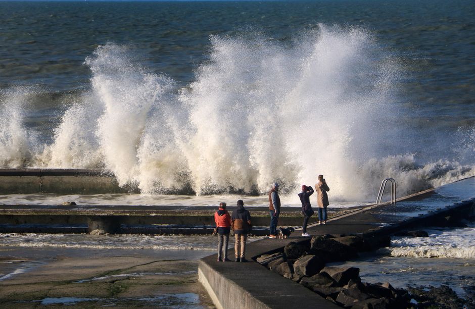Tourists watch crashing waves on the seashore at Saint-Pair-sur-Mer, Normandie, France.