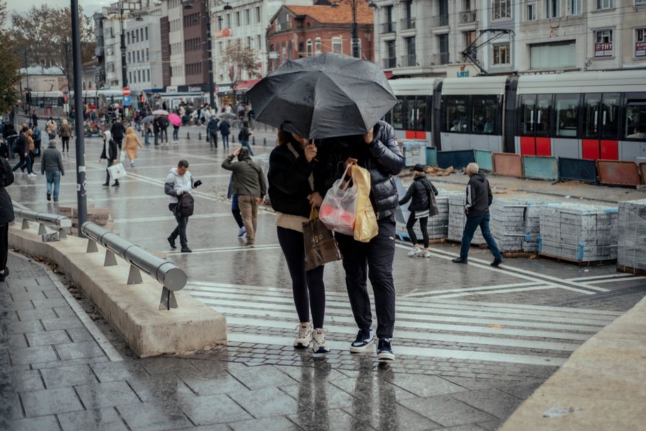 A bustling city street scene in the rain with people huddling under umbrellas.