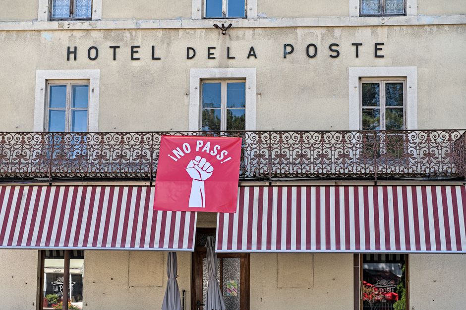 Hotel De La Poste facade with striking protest banner reading 'No Pass' in Val-de-Travers, Switzerland.