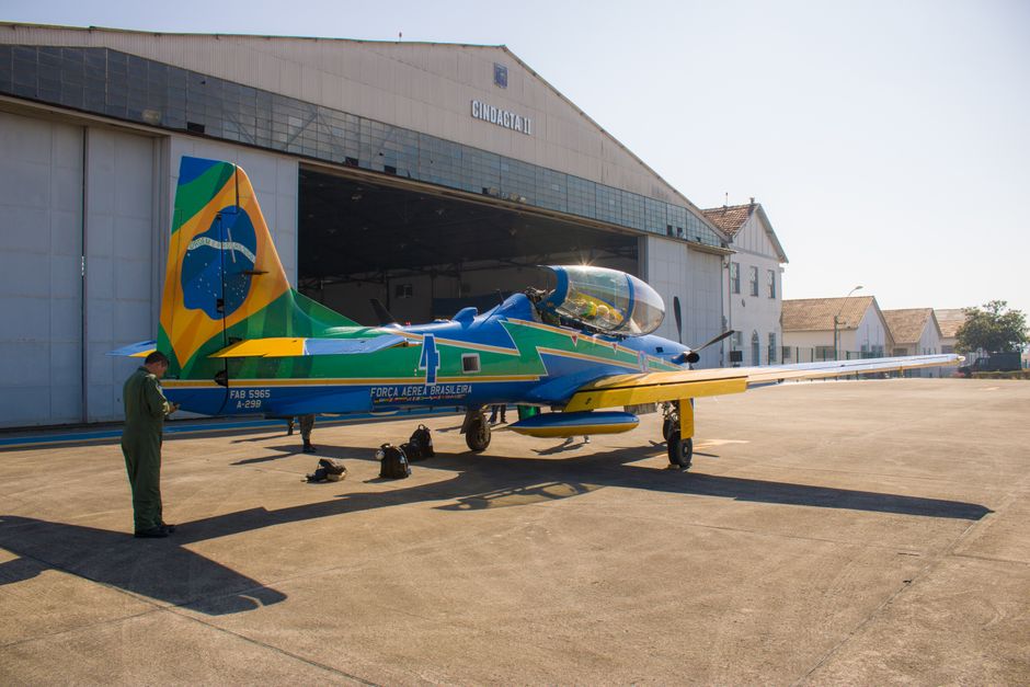 Brazilian Air Force aircraft parked outside a hangar with a military personnel on the tarmac.