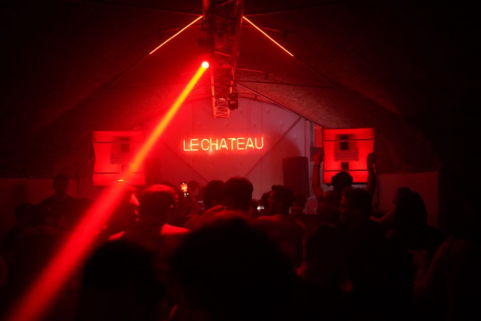 A lively crowd enjoys the nightlife under red neon lights at Le Chateau nightclub.