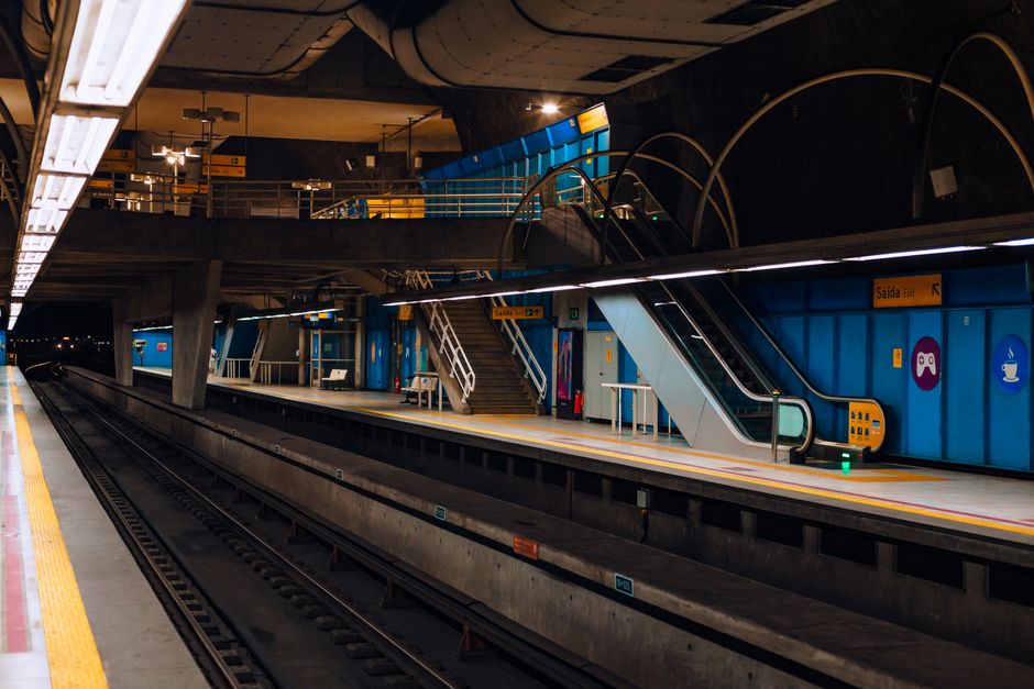An empty urban subway station platform with escalators and vibrant lighting at night.