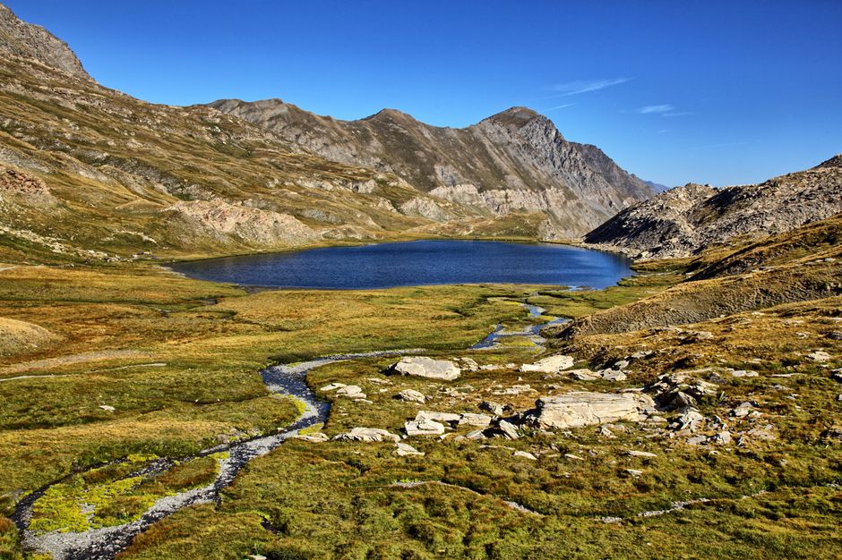 Breathtaking view of a mountain lake surrounded by rocky terrain and meadows in Molines-en-Queyras.