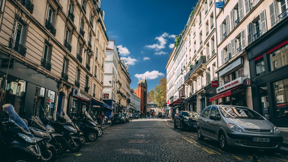 Picturesque Paris street scene featuring classic architecture, parked motorbikes, and cars.
