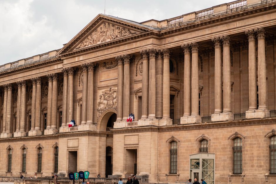 Front view of the iconic Louvre Museum facade, Paris, with French flags displayed.