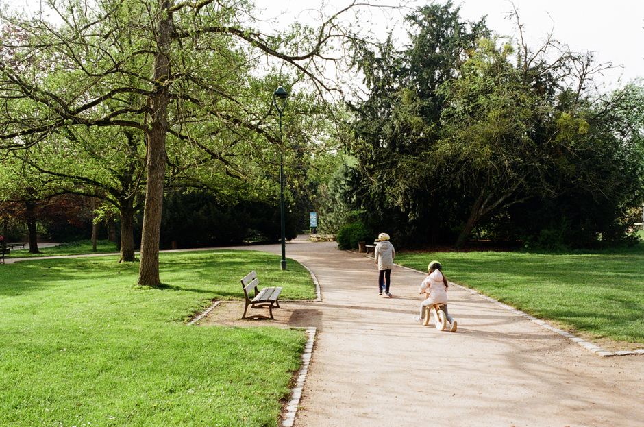 Two children enjoy a sunny day at a park in Nancy, France, surrounded by greenery and a walking path.