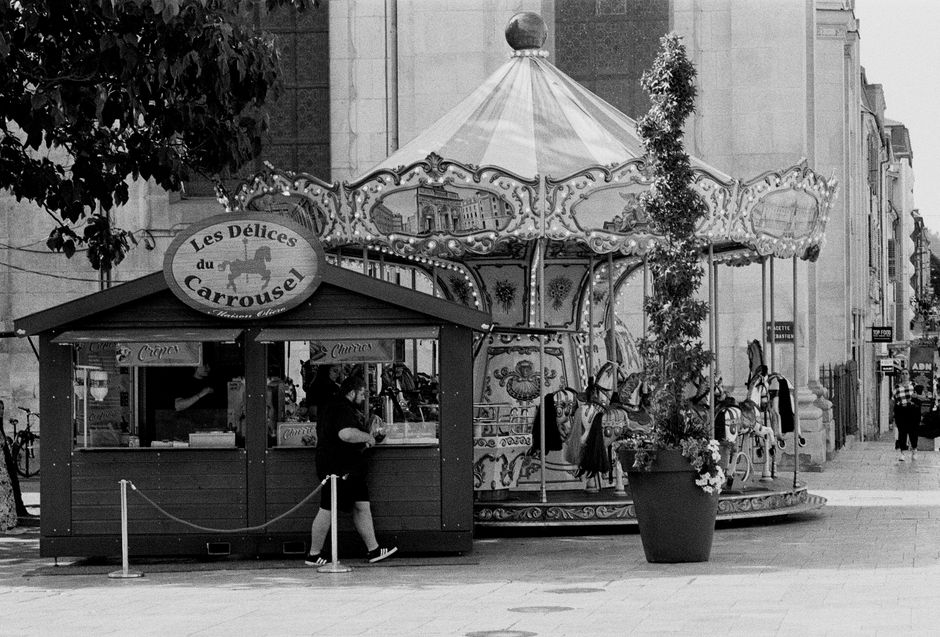 Black and white photo of a vintage carousel and food stand in Nancy, France.