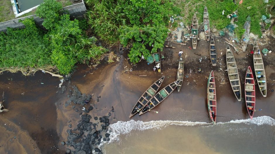Aerial view of canoes along Nicholls Island, Cameroon shoreline with lush greenery.