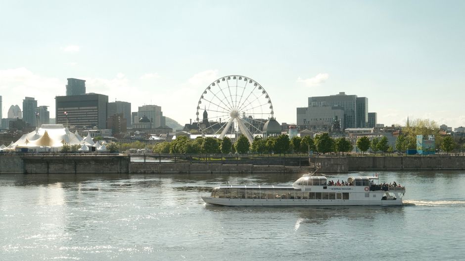 View of Montreal skyline with a river ferry and Ferris wheel on a sunny summer day.