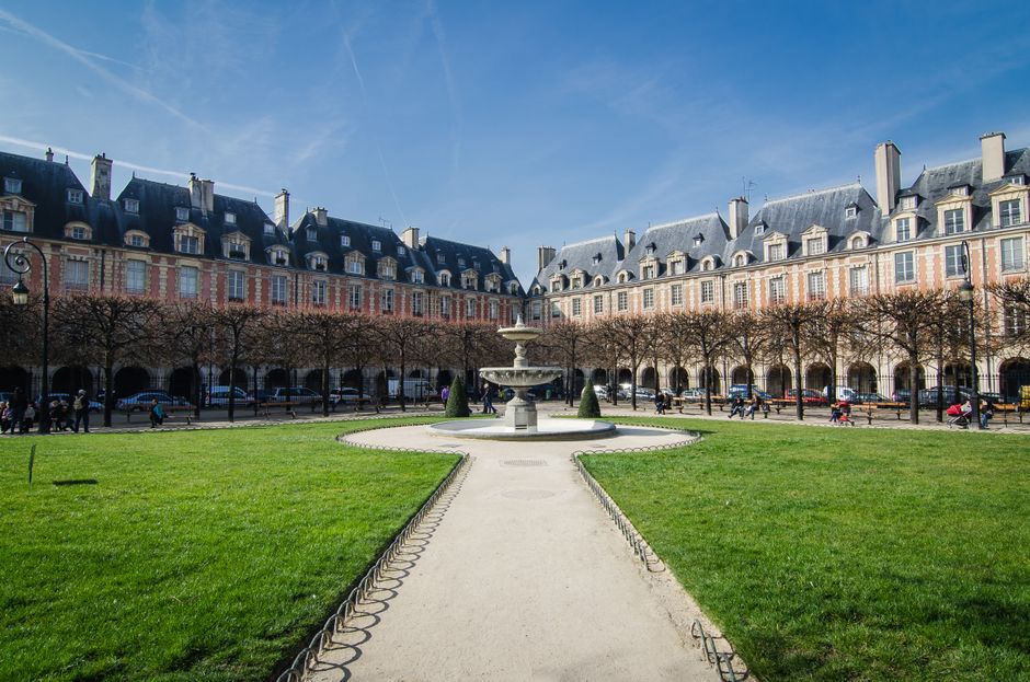 Beautiful day at Place des Vosges with fountain and historic architecture.