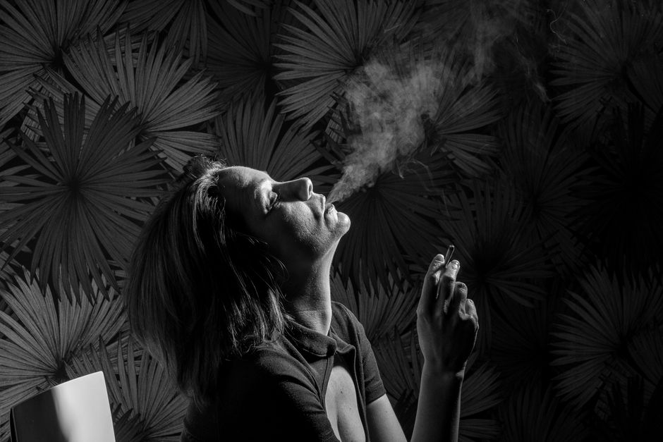 Elegant portrait capturing a woman exhaling smoke against a textured backdrop.