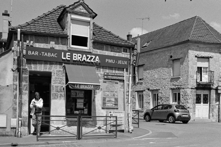 Black and white photo of a French street with 'Le Brazza' shop and a person standing at the entrance.
