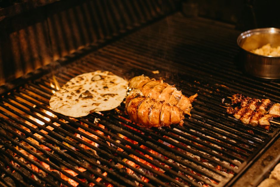 Close-up of meat and bread grilling on an outdoor BBQ with visible flames