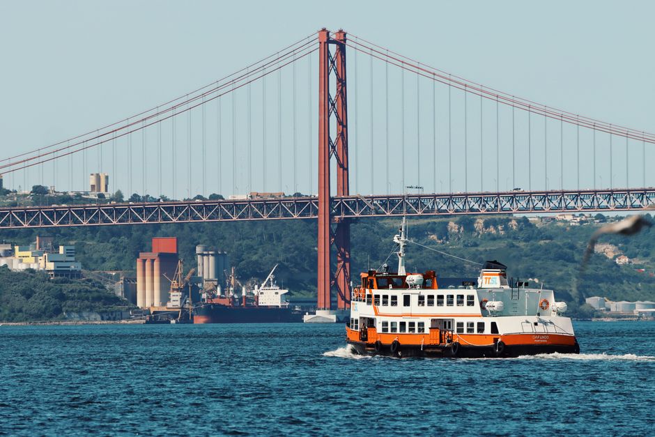 Scenic view of the iconic 25 de Abril Bridge in Lisbon with a ferry crossing the river.