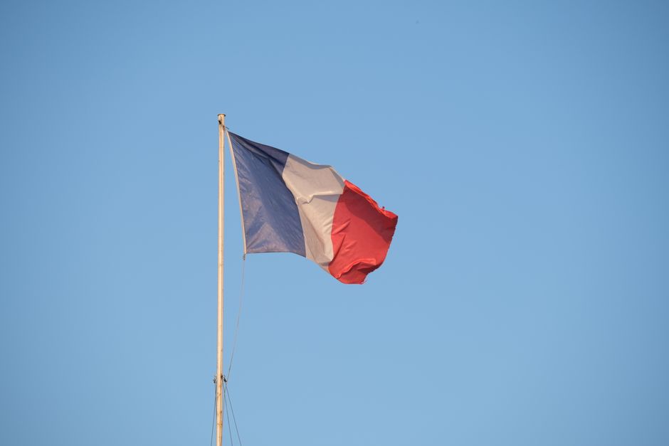 The French national flag waving on a flagpole against a clear blue sky.