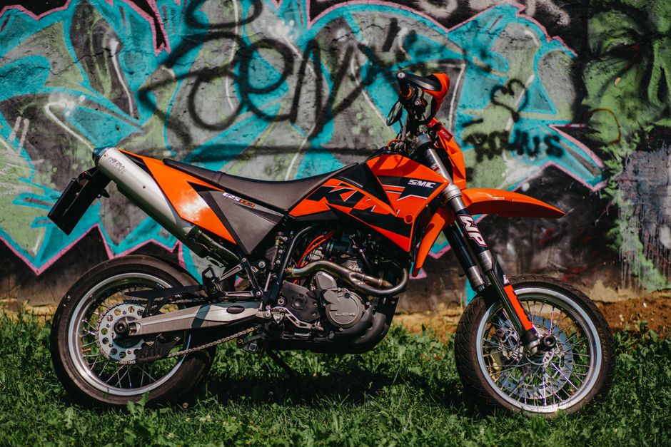 Orange KTM motorcycle parked against graffiti-covered wall, showcasing urban motorsport style.