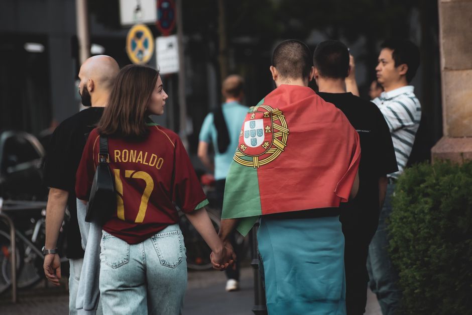 A group of football fans in Berlin, one wearing a Portugal flag, walking the street.