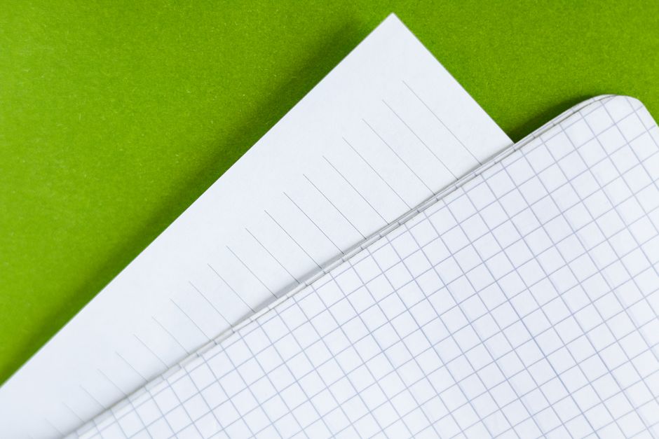 Detailed close-up of white lined and graph paper sheets on a vibrant green background.