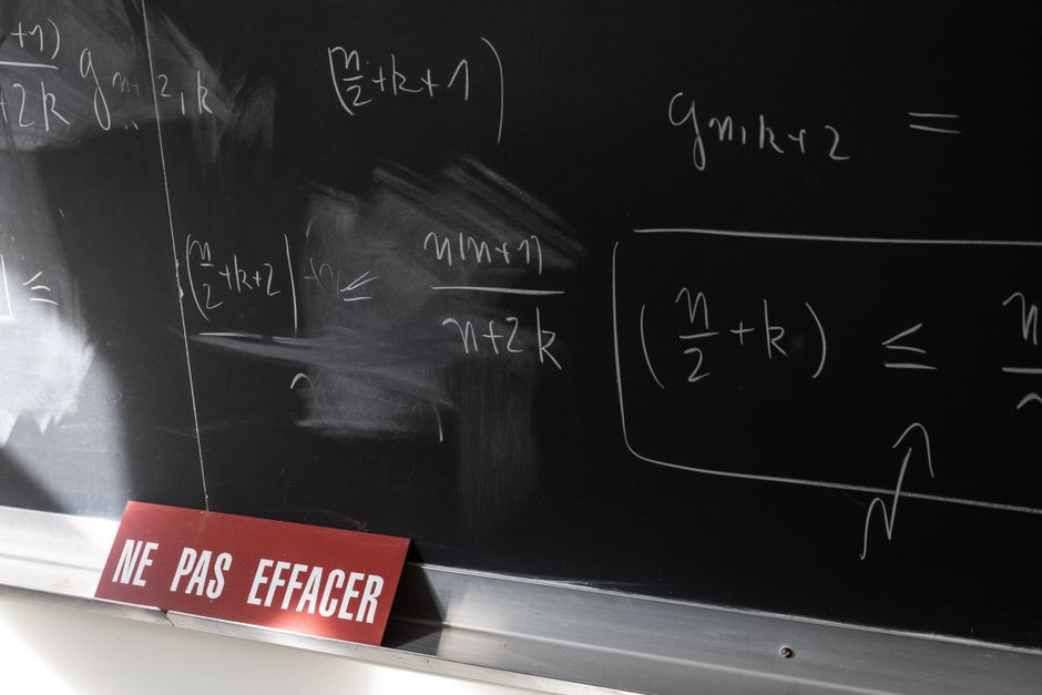 Chalkboard with math equations and French warning sign in a classroom setting.