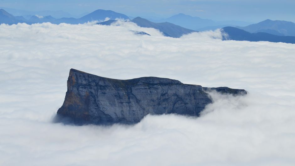 A breathtaking aerial view of a mountain peak surrounded by clouds in Gresse-en-Vercors, France.