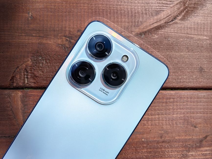 Close-up of a smartphone camera showing three lenses on a rustic wooden background.