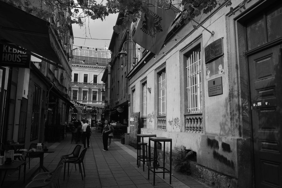 Black and white photo of a European alleyway lined with eateries and people.