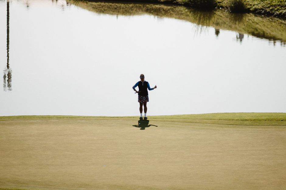A lone golfer stands by a tranquil lake, casting a silhouette on a bright day in Paris.
