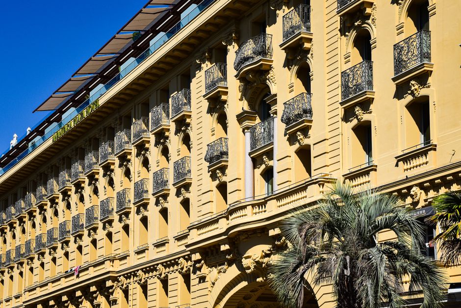 Beautiful historic building facade in Provence-Alpes-Côte d'Azur, France with intricate balconies and palm trees.