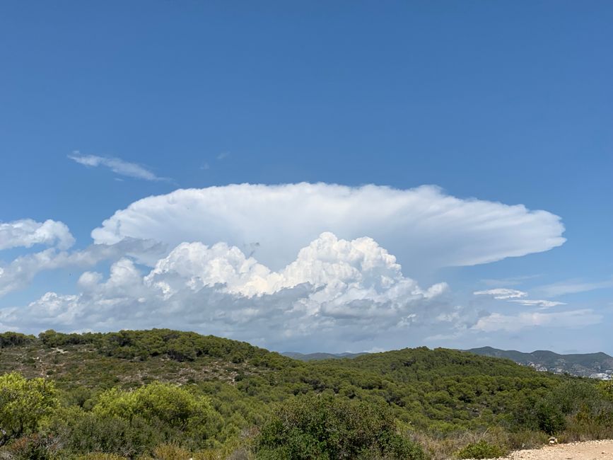 Stunning cumulonimbus cloud formation over lush green hills under a clear blue sky.