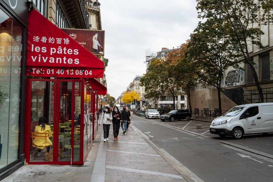 Vibrant Parisian street with a red awning cafe, pedestrians, and autumn foliage.