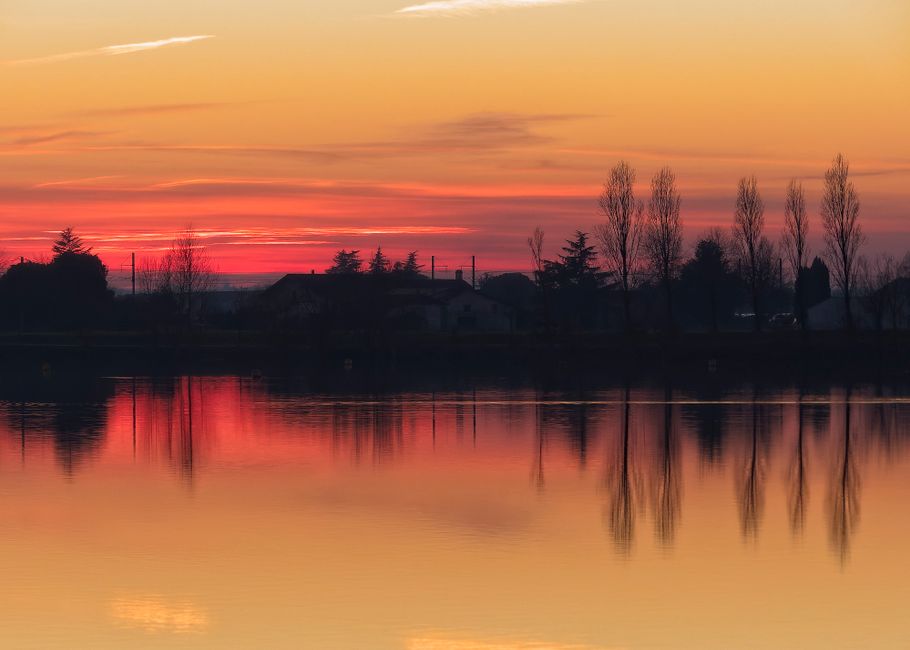 A peaceful sunset over a lakeside with calm water reflections and vibrant sky hues.