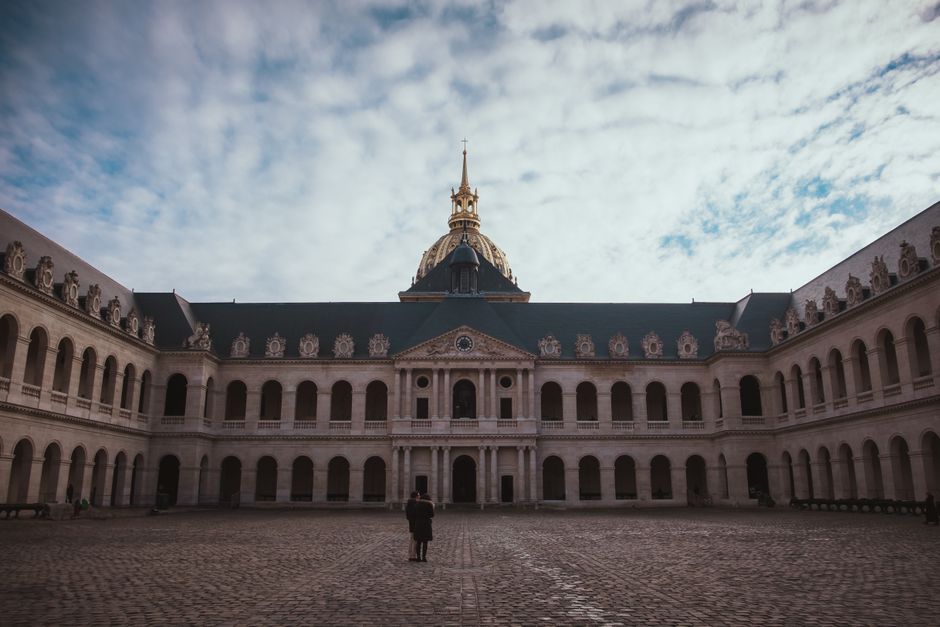 Historic courtyard of Les Invalides with a view of the chapel dome under a cloudy winter sky.
