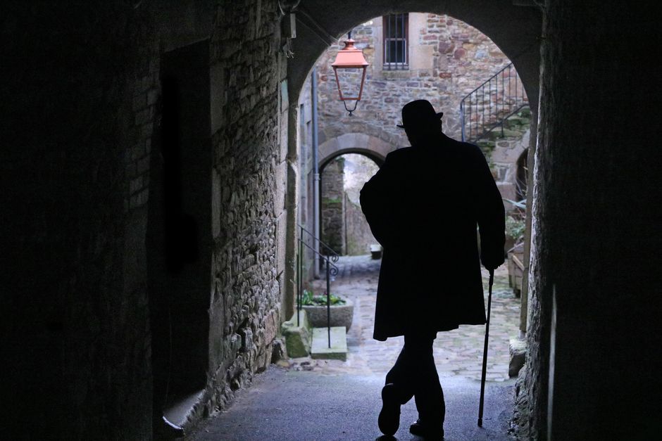 A silhouette of a man with a cane in a historic alley of Villedieu-les-Poêles, France.