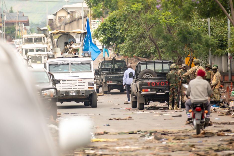 Urban scene with military presence and convoy of vehicles on a city street.