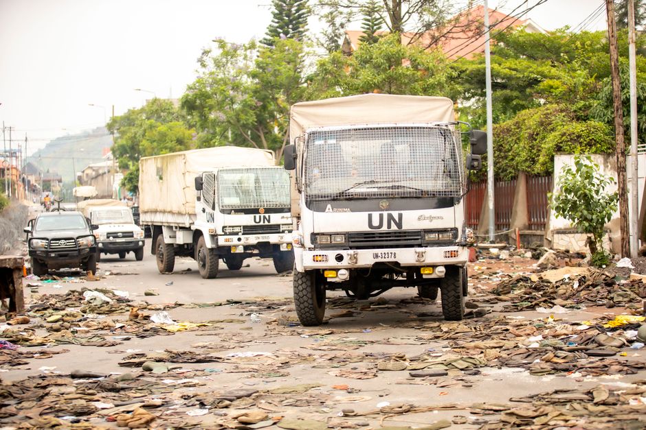 UN trucks travel through a debris-filled street, highlighting urban challenges.