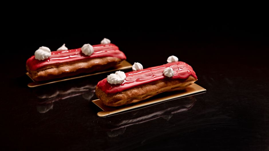 Exquisite red glazed eclairs with white cream decoration, artfully presented on a dark surface.