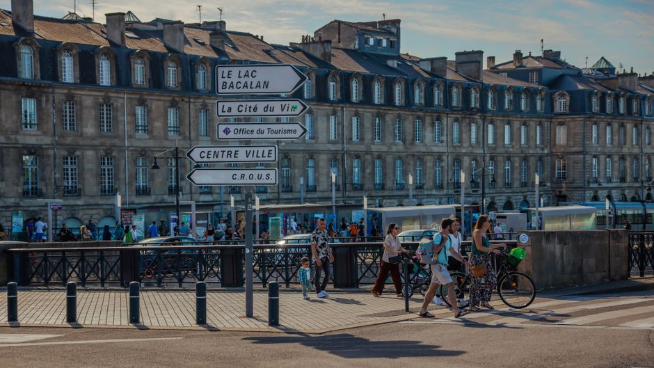 People walking near directional signs in Bordeaux, featuring historic architecture and bustling streets.