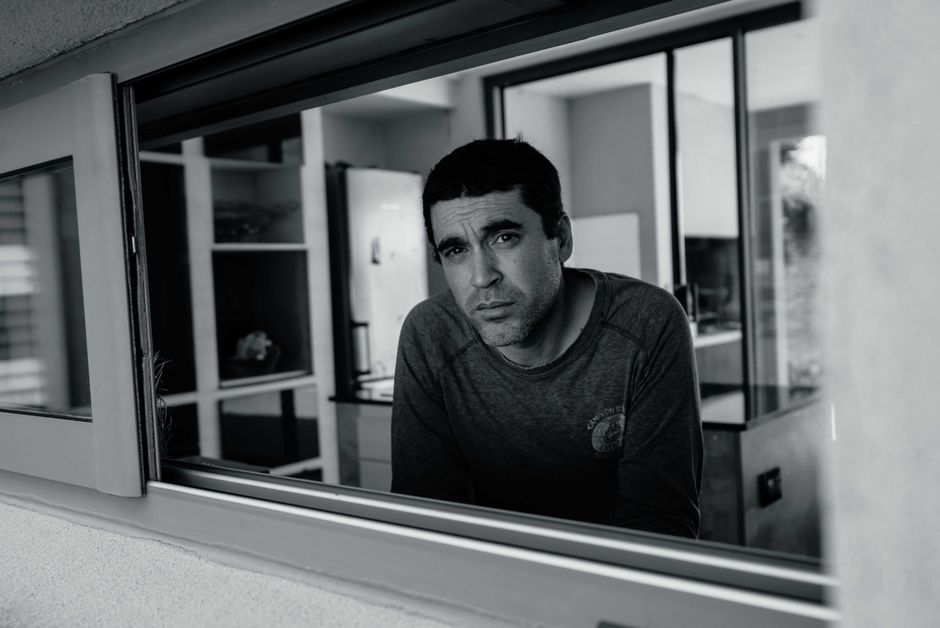 Black and white portrait of a pensive man gazing through a window into an indoor space.