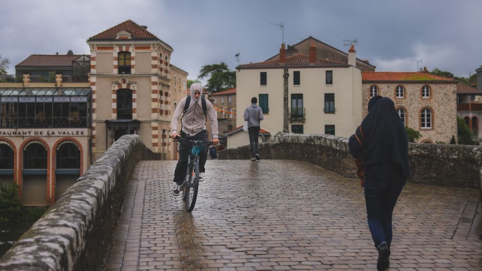 Man cycling on a historic bridge in Clisson, France on a cloudy day.