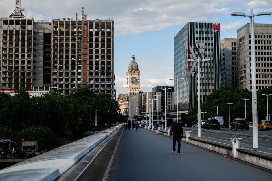 View of an urban bridge with pedestrians and a distant clock tower surrounded by tall buildings.