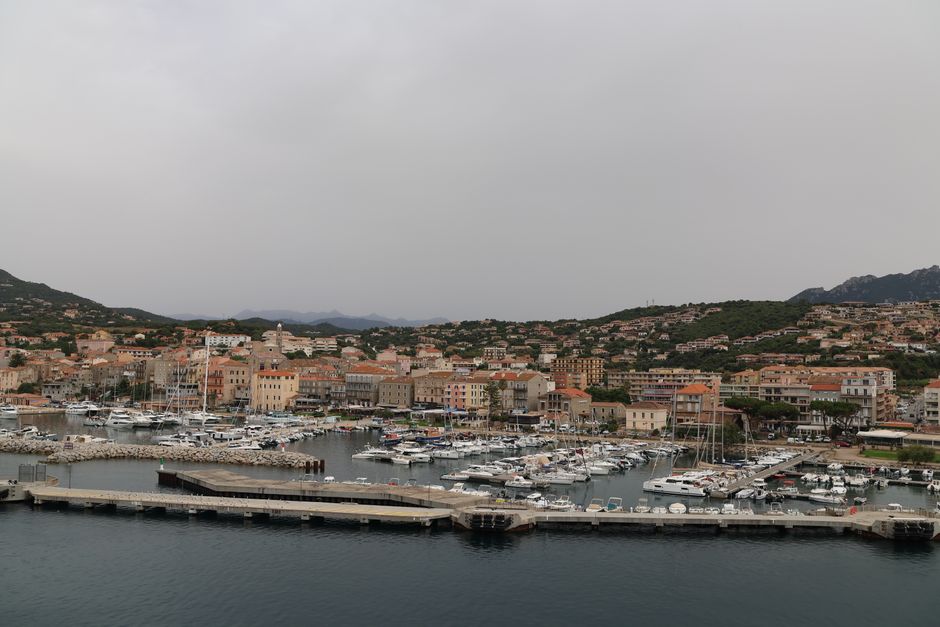 Scenic view of a harbor town with yachts moored at the marina, set against lush hills.