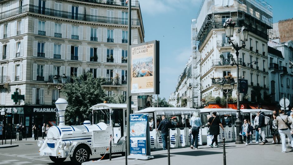 A vibrant street view in Montmartre, Paris with a tour train and bustling crowd.