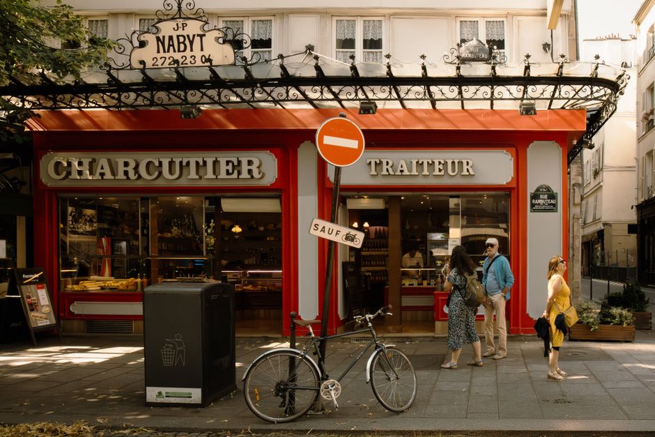 Parisian streetscape featuring a charcuterie and pedestrians in warm sunlight.