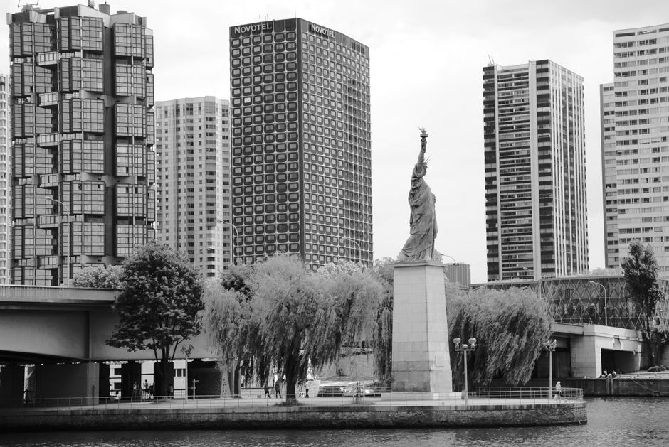 Black and white photograph of the Statue of Liberty replica with Paris cityscape in the background.
