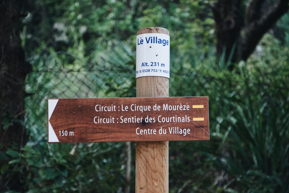 Wooden signpost in forest guiding to Le Cirque de Mourèze and Sentier des Courtinals.